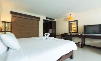 a clean , well - organized bedroom with a white bed , wooden furniture , and a television in the corner at Pattawia Resort & Spa, Pranburi