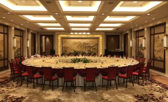 A spacious room is set up for an event, with long tables adorned with a centerpiece and surrounded by gold chairs at JinLing Purple Mountain Hotel Shanghai