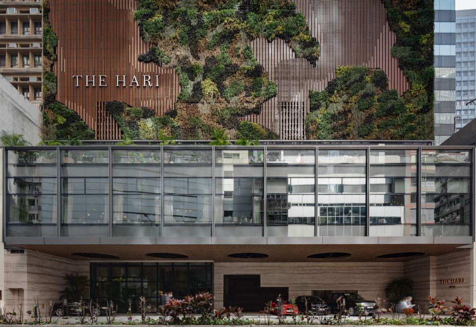 The front facade and entrance of a large building showcase an intriguing architectural feature on one side at The Hari Hong Kong