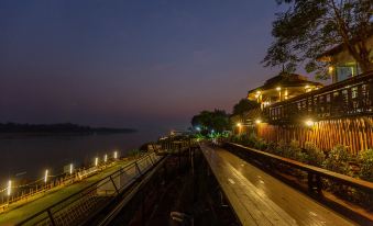 a boardwalk with a restaurant and trees , overlooking a body of water at night at Chiangkhan River Mountain Resort