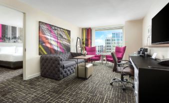 a modern living room with gray and pink furniture , a large window offering city views , and a cityscape visible through the window at Hyatt Centric Arlington