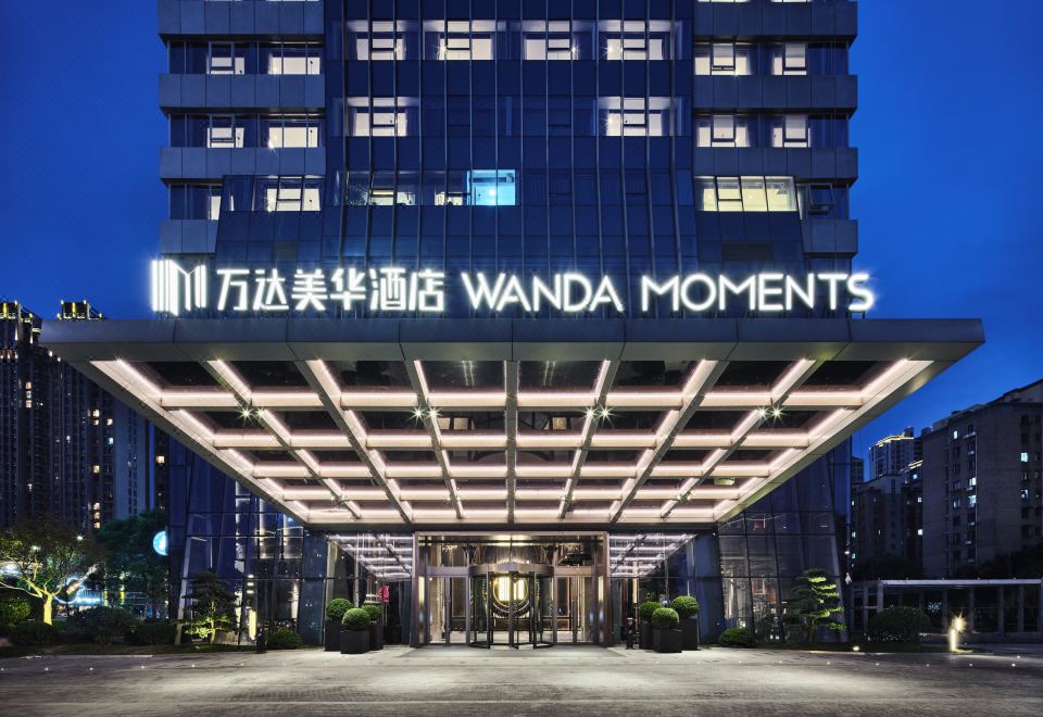 At night, a hotel entrance is adorned with an illuminated sign above its glass door at Wanda Moments