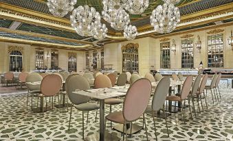 The dining room is elegantly furnished with tables, chairs, and chandeliers hanging from the ceiling at Hotel Alexandra
