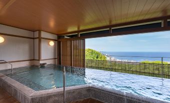 a large indoor pool with a view of the ocean through a window , surrounded by wooden walls at Kamenoi Hotel Atami Annex