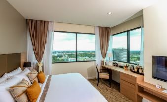 a spacious hotel room with a large window overlooking the city , featuring a bed , desk , and chair at Grand Fortune Hotel Nakhon Si Thammarat