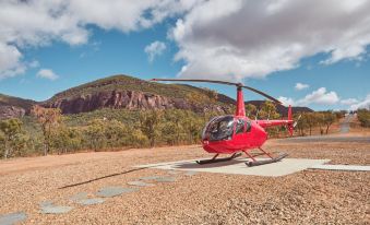 a red helicopter is parked on a dirt ground with mountains in the background , under a cloudy sky at Mt Mulligan Lodge