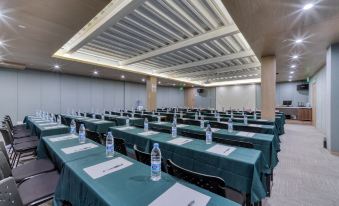A spacious event room is arranged with long tables and green chairs at the front at Weiting Century Hotel