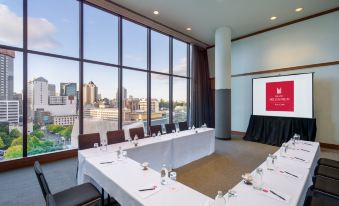 a conference room with a large table and chairs , a projector screen , and a view of the city at Grand Millennium Auckland