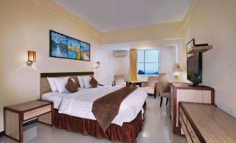 a large bed with white sheets and a brown blanket is in the center of a room at Aston Karimun City Hotel