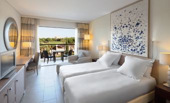 a hotel room with two beds , white linens , and large windows that offer views of the outdoors at Hilton Vilamoura As Cascatas Golf Resort & Spa