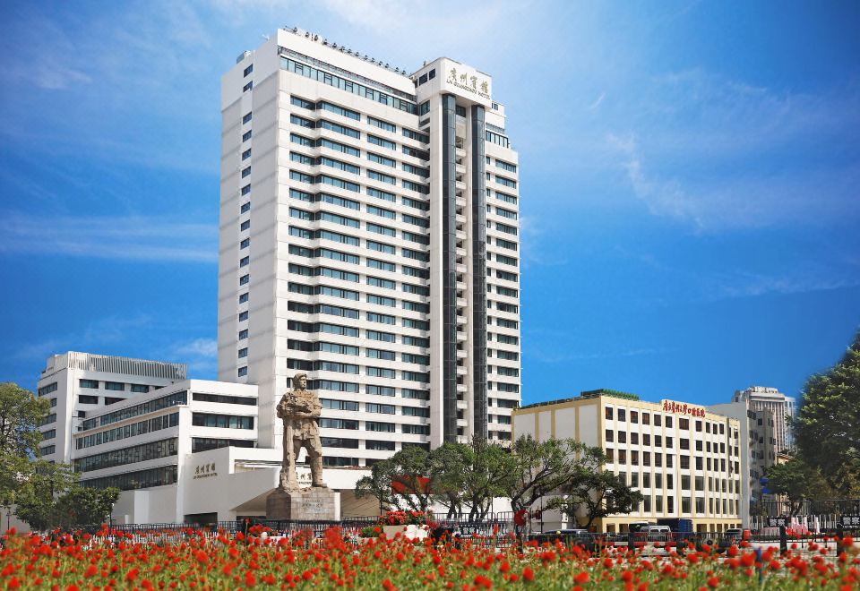 a tall white building with a statue in front of it and red flowers in the foreground at Guangzhou Hotel
