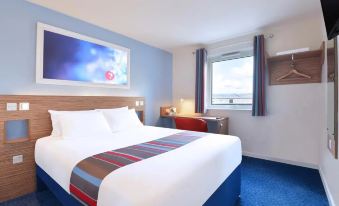a hotel room with a large bed , white linens , and a blue carpet , next to a window at Travelodge Porthmadog