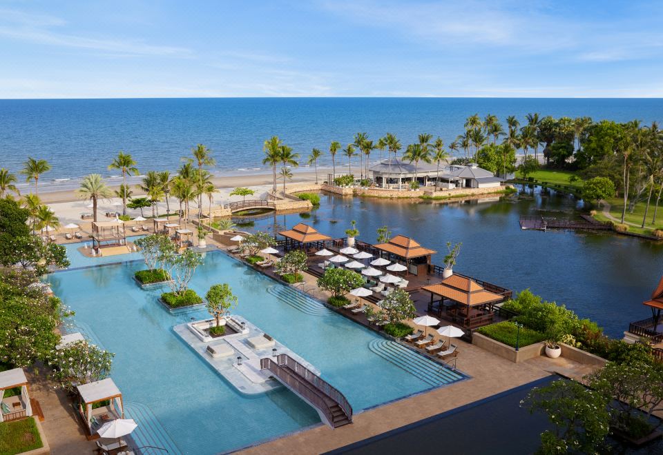 aerial view of a resort with a large pool surrounded by lounge chairs and umbrellas , situated near the ocean at Dusit Thani Hua Hin