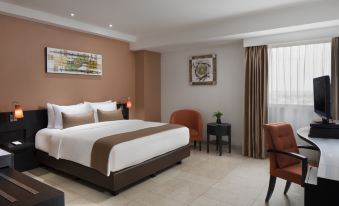 a large bed with white linens is in a room with orange chairs and a painting on the wall at Aryaduta Palembang