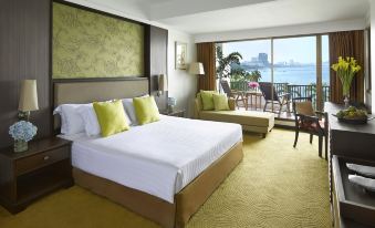 a large bed with white linens is in a room with a chair and a window overlooking the ocean at Dusit Thani Pattaya