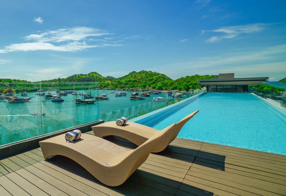 a large swimming pool surrounded by a wooden deck , with several lounge chairs placed around the pool at Meruorah Komodo Labuan Bajo