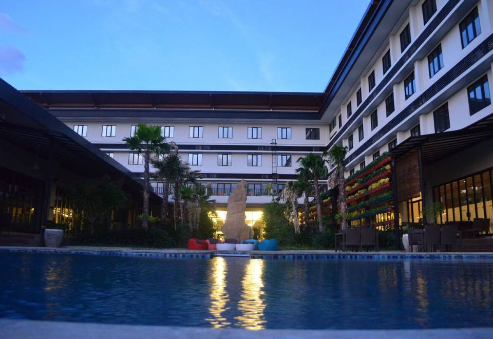 a large building with a swimming pool in front of it , surrounded by palm trees at Hotel Neo Eltari - Kupang by Aston
