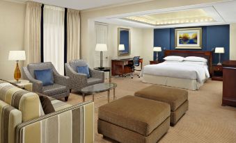 a modern hotel room with a large bed , comfortable seating area , and a desk , all lit by the sofas at Sheraton Skyline Hotel London Heathrow