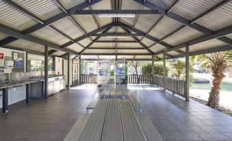 a large , open room with a metal roof and wooden flooring is filled with wooden benches at Nrma Sydney Lakeside Holiday Park