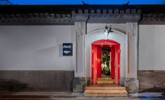 The entrance to a building with red doors and windows is illuminated at night, accompanied by ornate decorations at Peking Yard  Boutique Hotel