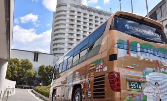 a large tour bus driving down a city street , surrounded by buildings and a blue sky at Kobe Portopia Hotel