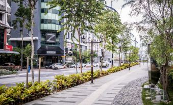 a city street with tall buildings on both sides , and a sidewalk lined with trees and bushes at Z Hotel