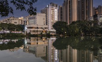 a large building is reflected in a calm lake with trees and buildings in the background at Atour Hotel