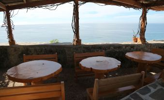 a restaurant with wooden tables and chairs , overlooking the ocean , under a shelter made of branches at Antulang Beach Resort