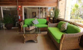 a cozy living room with green couches , a glass coffee table , and potted plants , under a wooden ceiling at Antulang Beach Resort