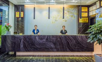 An employee stands next to the front desk in the hotel lobby, where there are people waiting at JinHao YiMei Hotel