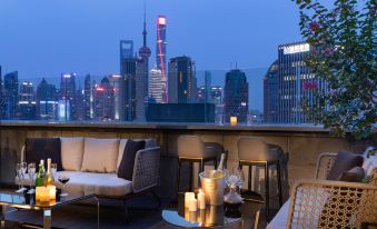 An upper floor room in the hotel offers a balcony with tables and chairs that overlook the city at night at Elegant Hotel Shanghai Bund