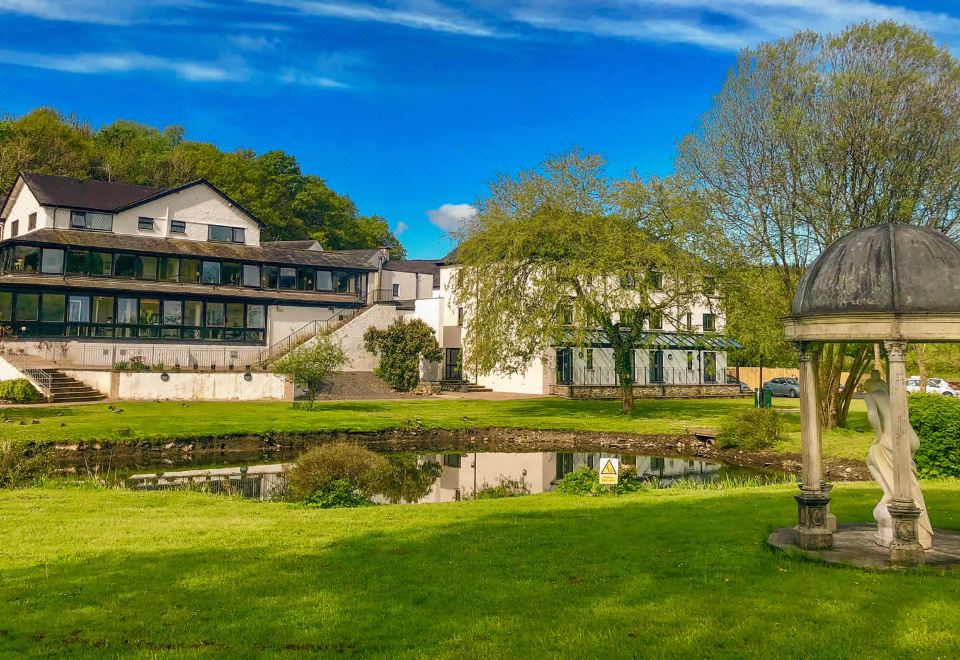 a large building with a pond in front of it , surrounded by trees and grass at Damson Dene Hotel