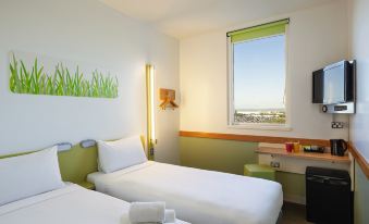 a modern hotel room with two beds , white bedding , and a window offering a view of the city at Ibis Budget Auckland Airport