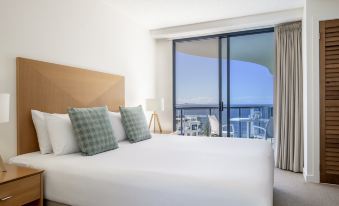 a large bed with white sheets and a wooden headboard is in a room with a view of the city at Mantra Mooloolaba Beach