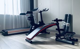 In the middle of the room, there is a gym area with an exercise bike and bench, accompanied by a small table with two chairs and a wall-mounted television at Shanghai JOYFUL YARD Hotel (Shanghai Pudong Airport Store)