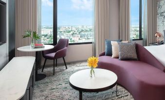 The living room features two chairs and a table, offering a scenic view of the city at night through its expansive windows at Avani Sukhumvit Bangkok Hotel
