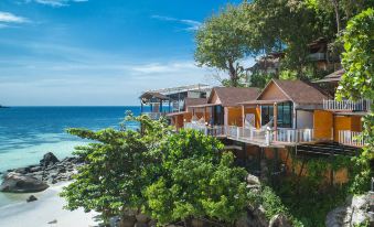 a wooden beach house situated on a cliff overlooking the ocean , with a balcony overlooking the water at Chareena Hill Beach Resort