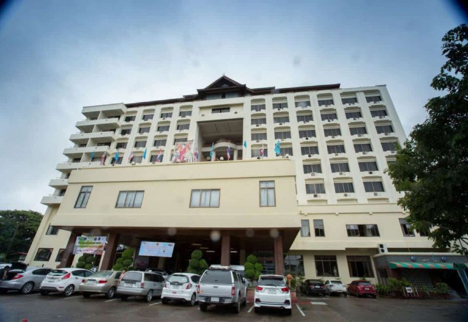 a tall building with a parking lot filled with cars and people in front of it at Phrae Nakara Hotel