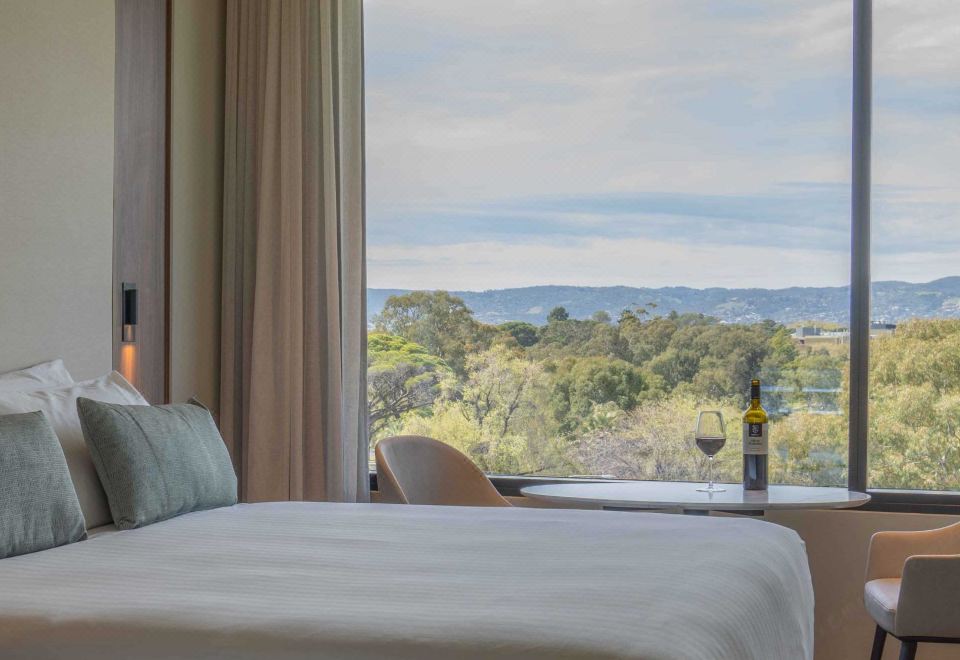 a hotel room with a large window overlooking a beautiful view of the mountains , and a bed with white sheets at Oval Hotel at Adelaide Oval, an EVT hotel