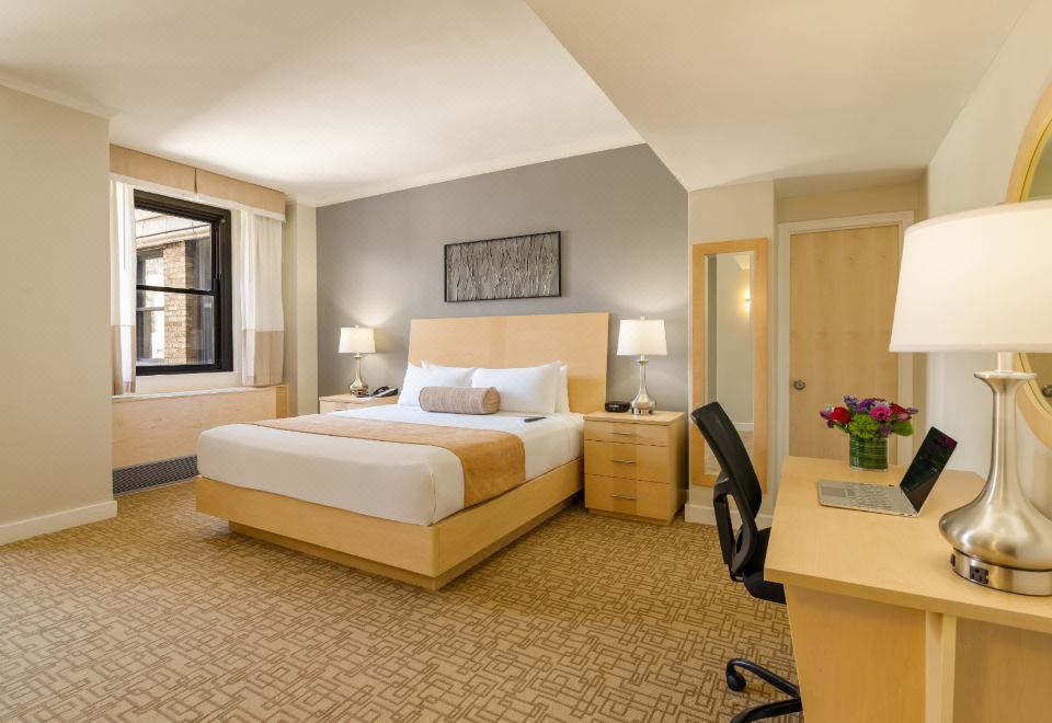 The bedroom features a large bed and a desk in the middle, as well as two full-size side tables at Hotel Pennsylvania