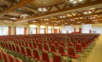 an empty auditorium with rows of red chairs and wooden beams on the ceiling , under bright lights at Unahotels Expo Fiera Milano