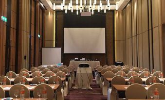 a conference room with rows of chairs and tables , a projector screen , and chandeliers hanging from the ceiling at Dusitd2 Khao Yai