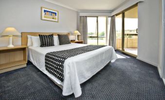 a well - decorated bedroom with a large bed , black and white checkered bedspread , and a sliding glass door leading to a balcony at Abbey Beach Resort