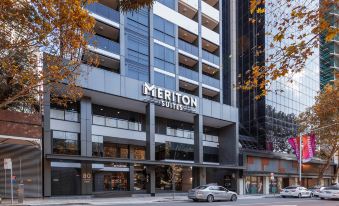 a modern building with the meriton suites logo , located in a bustling city environment with trees and cars at Meriton Suites North Sydney