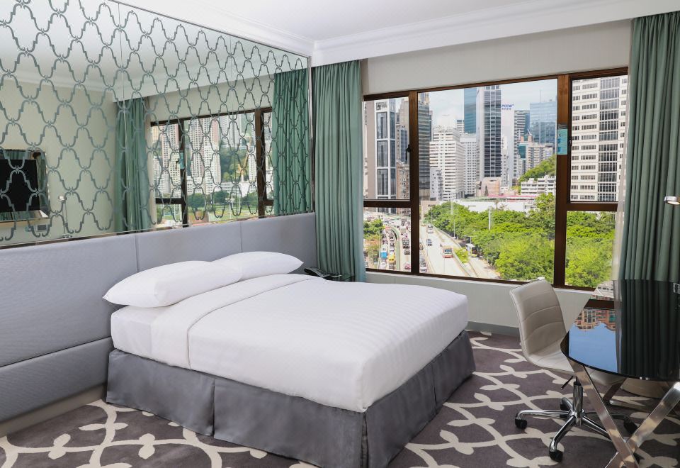 a large bed with white sheets and a gray headboard is in a room with a window overlooking a cityscape at Dorsett Wanchai
