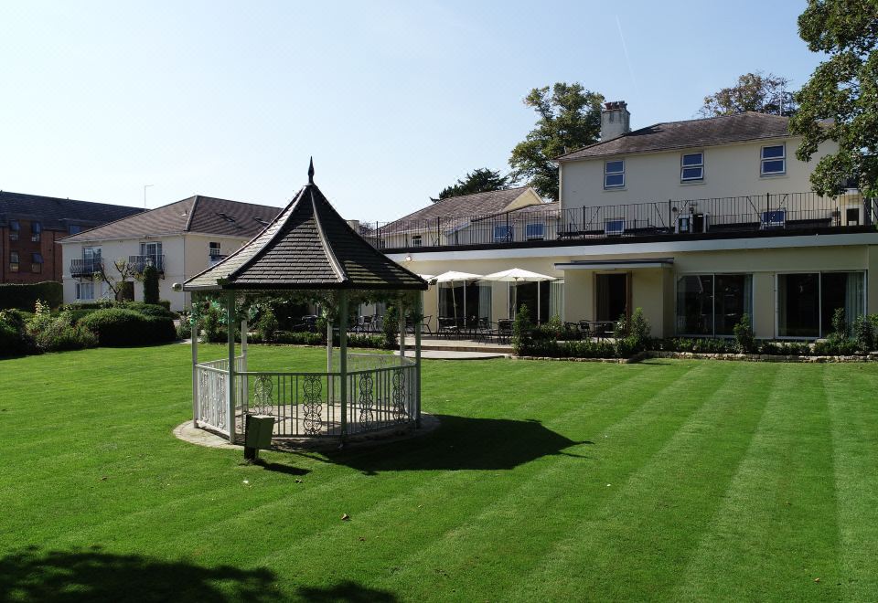 a large white gazebo is surrounded by green grass and bushes in front of a house at Alton House Hotel