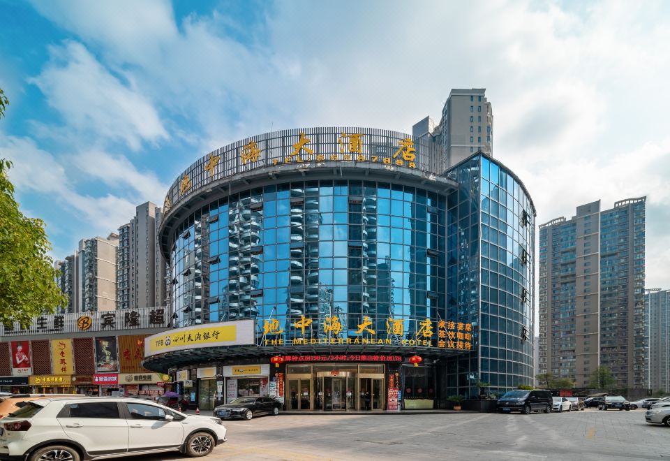 a large building with a glass facade and yellow signs is shown in front of other buildings at Mediterranean Hotel