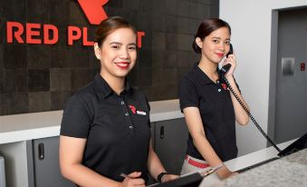 two women in black shirts are standing behind a counter , with one woman on the phone at Red Planet Manila Bay