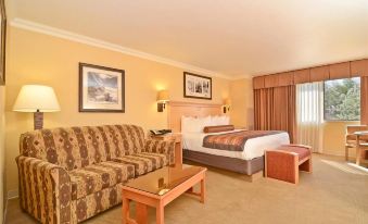 a hotel room with a king - sized bed , a couch , and a flat - screen tv . the room is well - lit and appears at Squire Resort at The Grand Canyon, BW Signature Collection