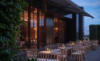 A waterfront restaurant with outdoor seating offers a scenic view of the water at night at Andaz Shenzhen Bay